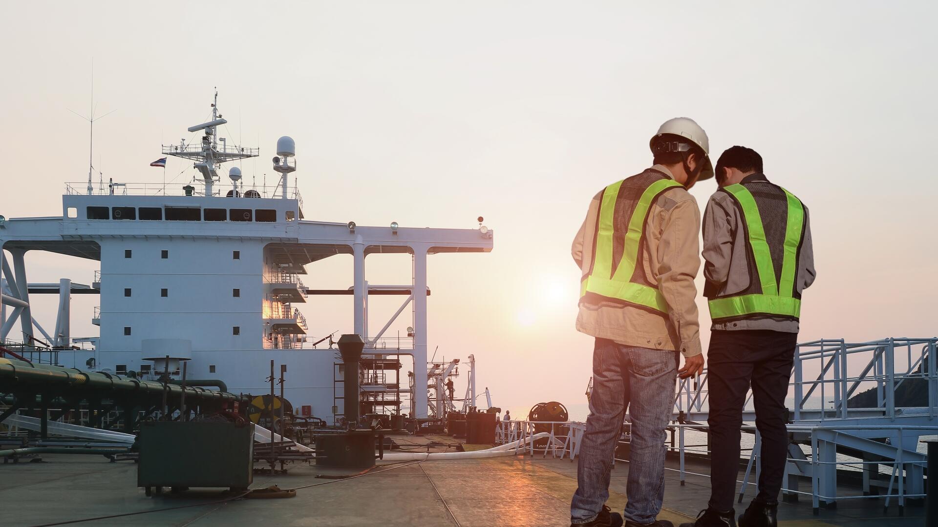 2 people in hi-vis vests, looking at a plan, on deck of container ship